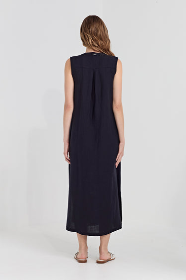 A woman viewed from the back wearing a sleeveless dark navy dress by Verge with a gathered back detail, standing against a light gray studio background.
