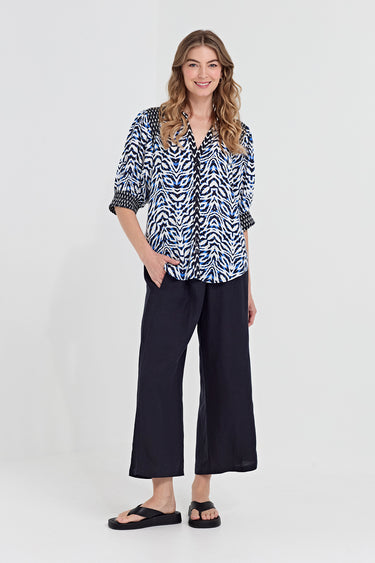 A woman wearing a blue, black, and white abstract patterned blouse by Verge with three-quarter sleeves, standing against a solid gray background.