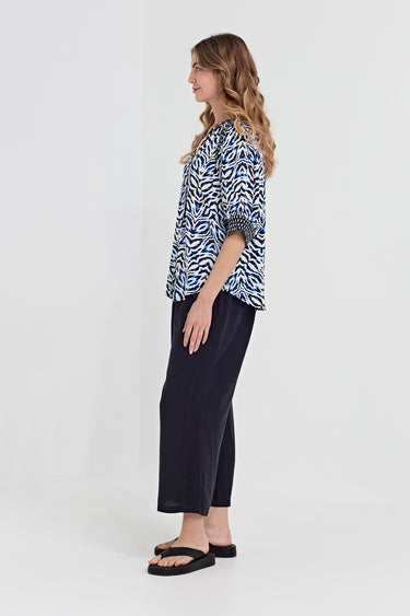 A woman wearing a blue, black, and white abstract patterned blouse by Verge with three-quarter sleeves, standing against a solid gray background.