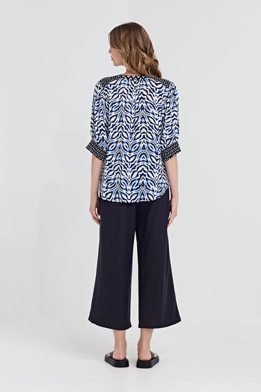 A woman wearing a blue, black, and white abstract patterned blouse by Verge with three-quarter sleeves, standing against a solid gray background.
