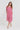 A woman modeling a short-sleeve midi dress by Verge with a pink and white abstract wavy pattern, standing against a plain light gray studio background.