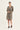 A woman modeling a long-sleeve, knee-length button-front dress by Verge with an allover snakeskin print in beige, brown, and black, paired with black slide sandals, against a plain white studio background.