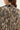 Close-up back view of a woman wearing a beige and black snakeskin print blouse by Verge with a small black fabric tab at the collar.