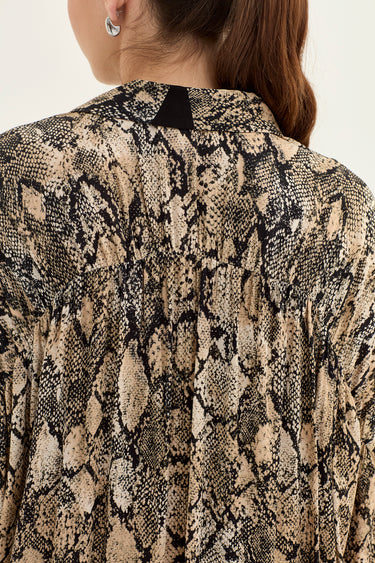 Close-up back view of a woman wearing a beige and black snakeskin print blouse by Verge with a small black fabric tab at the collar.