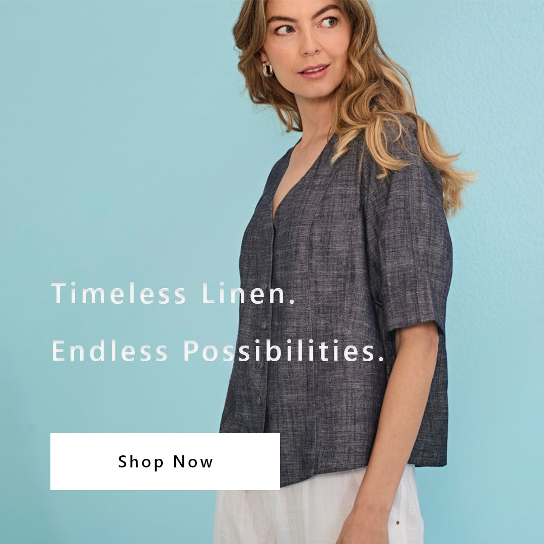 A woman wearing a dark gray linen short-sleeve top by Verge stands against a light blue background with text reading 'Timeless Linen. Endless Possibilities.