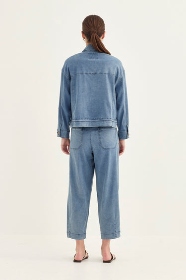 A model viewed from the back wearing a light blue denim jacket and matching cropped wide-leg denim pants by Verge, paired with black sandals, against a plain off-white studio background.