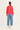 A model viewed from the back wearing a coral-red long-sleeve knit sweater, light-wash wide-leg blue jeans by Verge, and white sneakers against a plain off-white studio background.