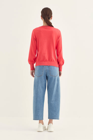 A model viewed from the back wearing a coral-red long-sleeve knit sweater, light-wash wide-leg blue jeans by Verge, and white sneakers against a plain off-white studio background.