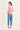 A woman is shown from the back wearing a light pink long-sleeve knit sweater with a scalloped hem and light blue cropped jeans by Verge, standing against a plain off-white studio background.