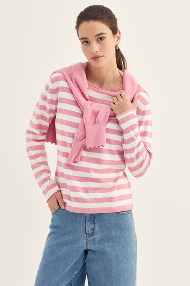 A woman modeling a pink and white striped long-sleeve top with a matching pink knit sweater by Verge draped over the shoulders, paired with blue jeans, against a plain light background.