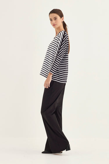 A woman modeling a black and white horizontally striped long-sleeve top with black wide-leg pants by Verge, standing in profile against a plain white studio background.