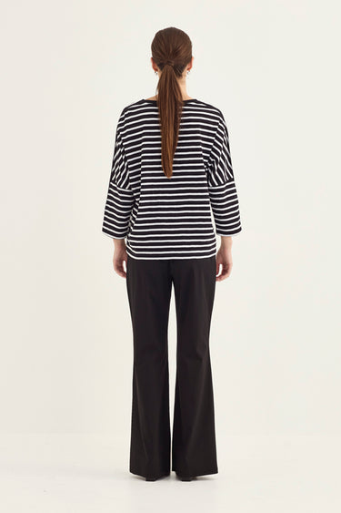 A woman viewed from the back wearing a black and white horizontally striped long-sleeve top and black wide-leg pants by Verge, standing against a plain light background.
