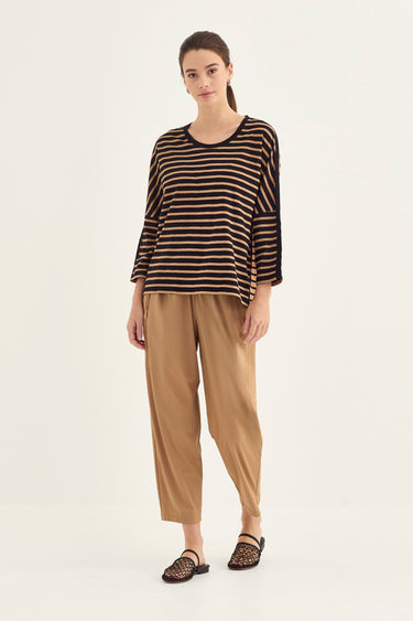 A woman modeling a three-quarter sleeve top with horizontal black and beige stripes, paired with beige cropped pants by Verge and black woven sandals, against a plain light background.