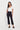 A woman modeling a white short-sleeve scoop-neck top and black cropped wide-leg pants by Verge with black sandals, standing against a plain white studio background.