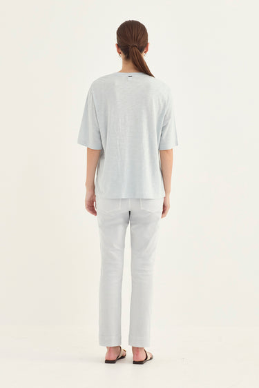 A woman viewed from the back wearing a light gray short-sleeve t-shirt and matching light gray pants by Verge, standing against a plain white studio background.