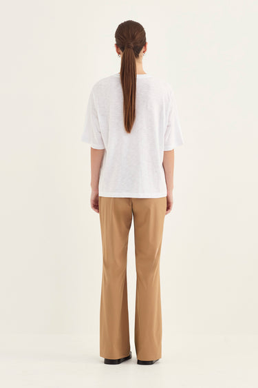 A woman viewed from the back wearing a white short-sleeve top and tan wide-leg pants by Verge against a plain light background.