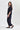 A woman modeling a dark navy blue two-piece lounge set consisting of a short-sleeve top and matching wide-leg pants  by Verge, paired with dark slip-on flats, against a light gray studio background.