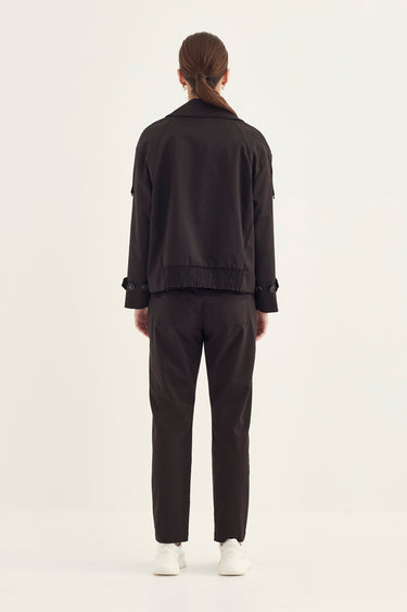 A model viewed from the back wearing a black cropped jacket with sleeve tabs and black trousers by Verge, paired with white sneakers by Verge, against a plain white studio background.