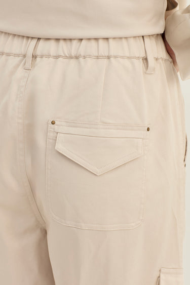 Close-up of the back waistband and pocket area of light beige or cream-colored pants by Verge, showing an elastic waist, belt loops, and a flap pocket with small metal rivets.