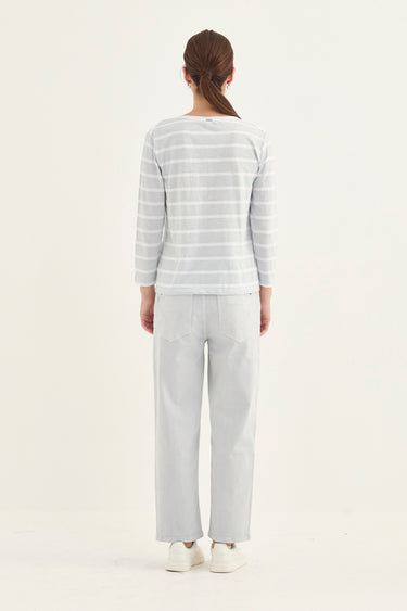 A woman viewed from behind wearing a light gray and white striped long-sleeve top with light gray wide-leg pants and white sneakers by Verge, set against a plain white studio background.