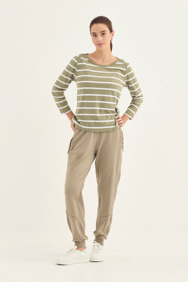 A woman modeling a two-piece loungewear set consisting of a long-sleeve top with horizontal olive green and white stripes, paired with relaxed-fit beige jogger pants by Verge and white sneakers, against a plain white studio background.