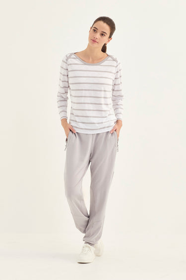 A woman modeling a light gray and white striped long-sleeve top with matching light gray jogger pants by Verge and white sneakers, standing against a plain white studio background.
