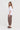 A woman modeling a white short-sleeve top and brown textured cropped pants with dark brown sandals by Verge, standing against a plain light gray studio background.