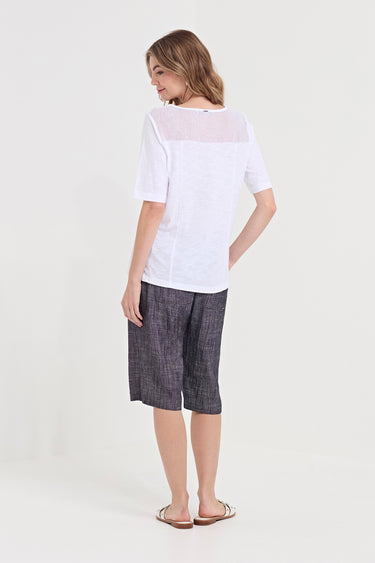 A woman shown from the back wearing a white short-sleeve top with a sheer yoke and dark gray plaid cropped shorts by Verge, standing against a plain light background.