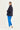 A woman modeling a dark navy blue lightweight jacket, paired with bright blue sweatpants by Verge and white sneakers, photographed from the back against a plain white studio background.