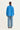 A model viewed from the back wearing a bright blue long-sleeve utility jacket and light blue wide-leg jeans by Verge against a plain off-white studio background.