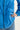 Close-up of a person wearing a blue lightweight jacket by Verge, showing the front zipper, gathered elastic detail, flap pocket, and hand tucked into the pocket.