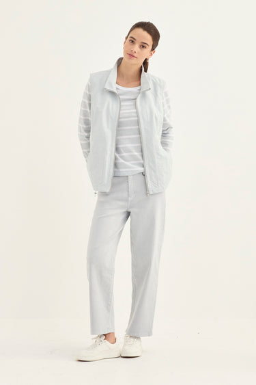 A woman modeling a light gray three-piece outfit consisting of a zip-up jacket, a horizontally striped long-sleeve top, and matching straight-leg trousers by Verge, paired with white sneakers against a plain white studio background.