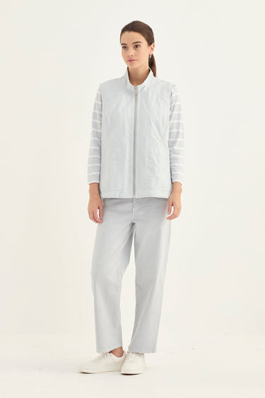 A woman modeling a light gray zip-up vest with sheer striped sleeves, paired with light gray trousers by Verge and white sneakers, against a plain white studio background.