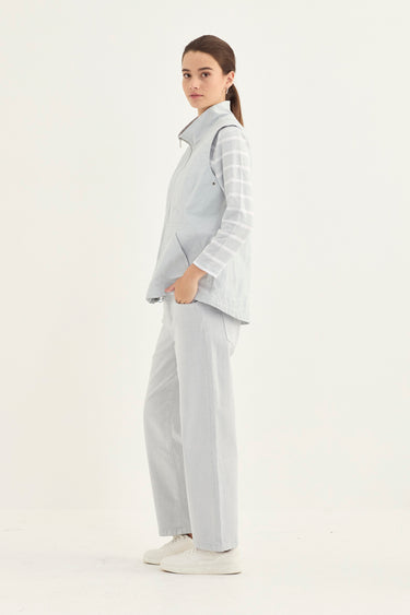 A woman modeling a light gray sleeveless vest and matching wide-leg trousers with striped long sleeves by Verge, standing against a plain white studio background.