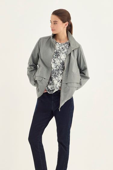A woman modeling a light gray zip-up jacket over a snake print jacket pattern, paired with dark navy jeans by Verge, against a plain off-white studio background.