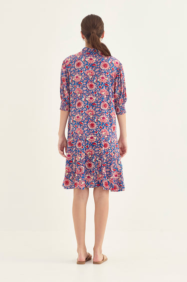 A woman viewed from the back wearing a knee-length floral shirt dress by Verge with three-quarter sleeves, on a plain light background.