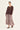 A woman modeling a dark brown long-sleeve top paired with a high-waisted, pleated maxi skirt featuring a dusty rose and beige paisley pattern by Verge, set against a plain off-white studio background.