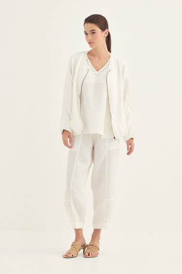 A woman modeling a white three-piece linen set consisting of a cropped jacket, a V-neck top, and cropped pants by Verge, paired with beige sandals, against a plain white studio background.