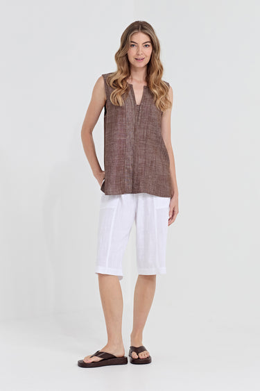 A woman modeling a sleeveless brown textured linen vest with a split neckline, paired with white linen shorts by Verge and dark brown sandals, against a light gray studio background.