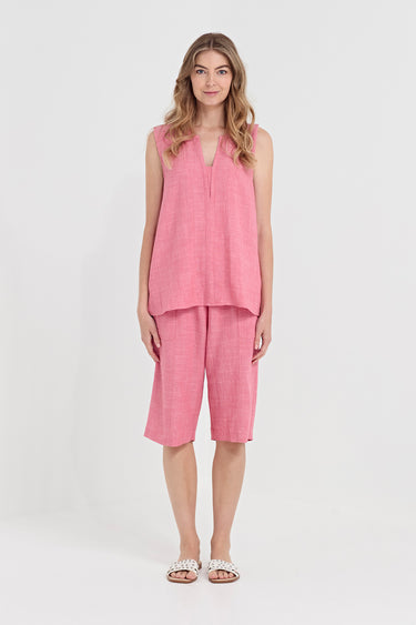 A woman modeling a two-piece pink linen set consisting of a sleeveless V-neck top and matching shorts by Verge, paired with white slide sandals, against a plain white studio background.