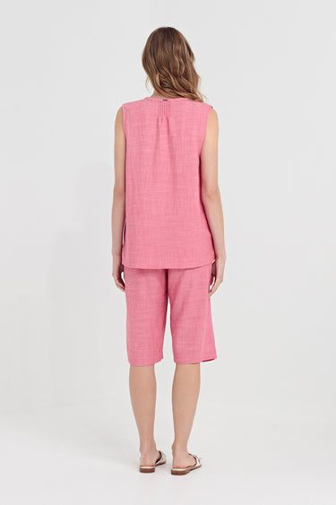 A woman viewed from behind wearing a pink sleeveless top and matching pink cropped shorts by Verge against a plain light gray studio background.