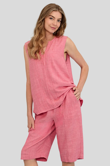 A woman modeling a sleeveless pink linen-like two-piece outfit with a cropped top and matching shorts by Verge against a light blue studio background.