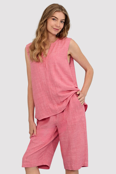 A woman modeling a sleeveless pink linen-like two-piece outfit with a cropped top and matching shorts by Verge against a light blue studio background.