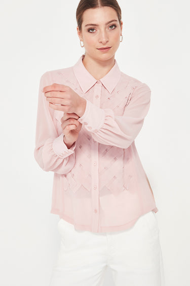 Woman wearing a light pink blouse with a subtle pattern by Verge on a white background