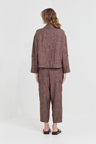 A model viewed from the back wearing a matching brown and beige plaid two-piece set consisting of a cropped long-sleeve jacket and cropped pants by Verge, paired with dark brown flat shoes, against a plain light gray background.