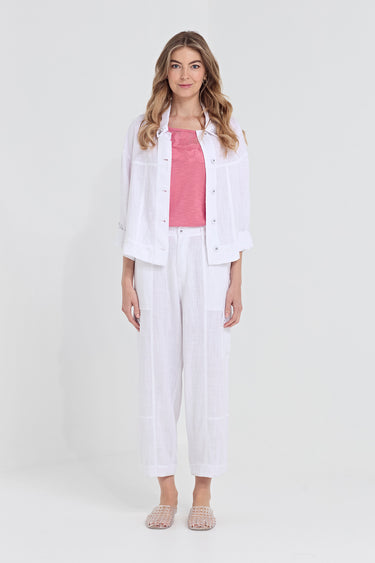 A woman modeling a white linen button-up jacket and matching white linen cropped pants, styled with a pink top by Verge and clear flat sandals, against a light gray studio background.