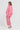A woman modeling a pink two-piece linen pajama set, featuring a long-sleeve button-up top and matching cropped pants  by Verge, shown from a side-back angle against a plain white studio background.