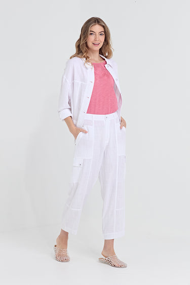 A woman modeling a white button-up shirt, white cropped pants by Verge, and a pink knit top against a plain light gray studio background.