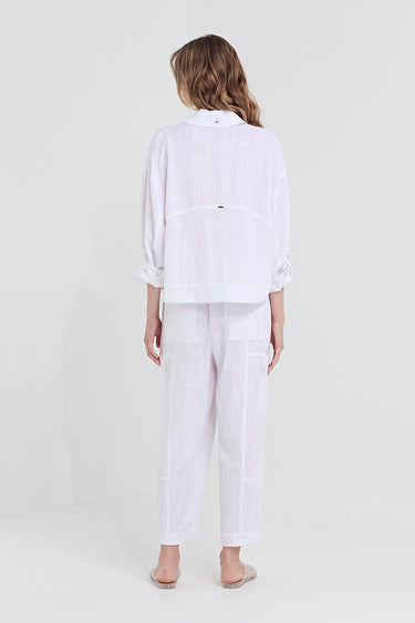 A woman viewed from the back wearing a white long-sleeve button-up shirt and matching white wide-leg trousers by Verge, standing against a plain light gray studio background.