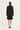 A model viewed from the back wearing a black tailored blazer and matching shorts set by Verge, with small gold chain details visible on the shoulders, against a plain off-white studio background.